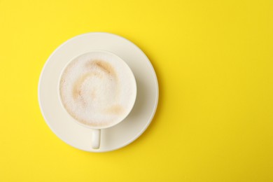 Tasty cappuccino in coffee cup on yellow background, top view. Space for text