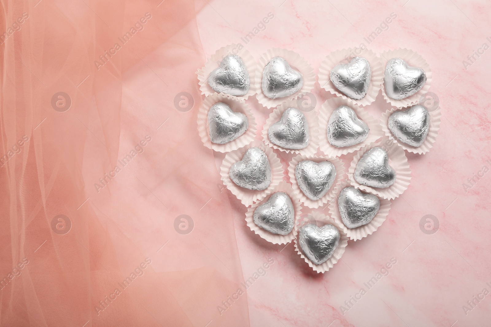 Photo of Heart made with delicious chocolate candies on pink background, top view. Space for text