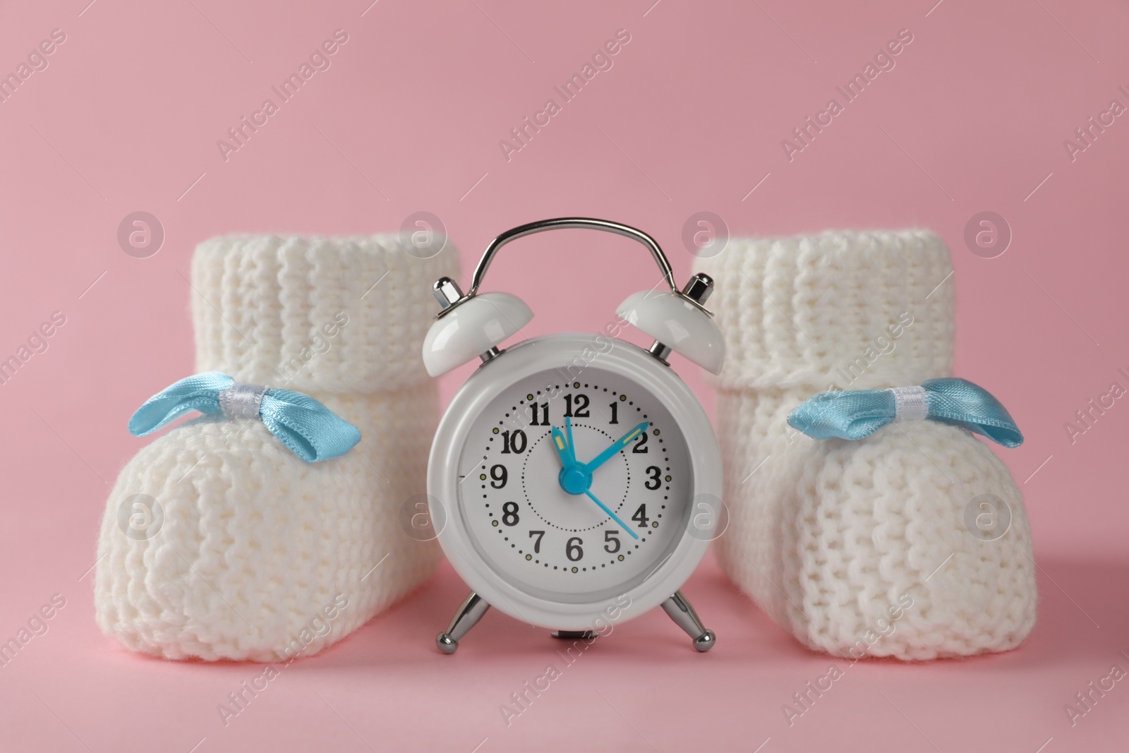 Photo of Alarm clock and baby booties on pink background. Time to give birth