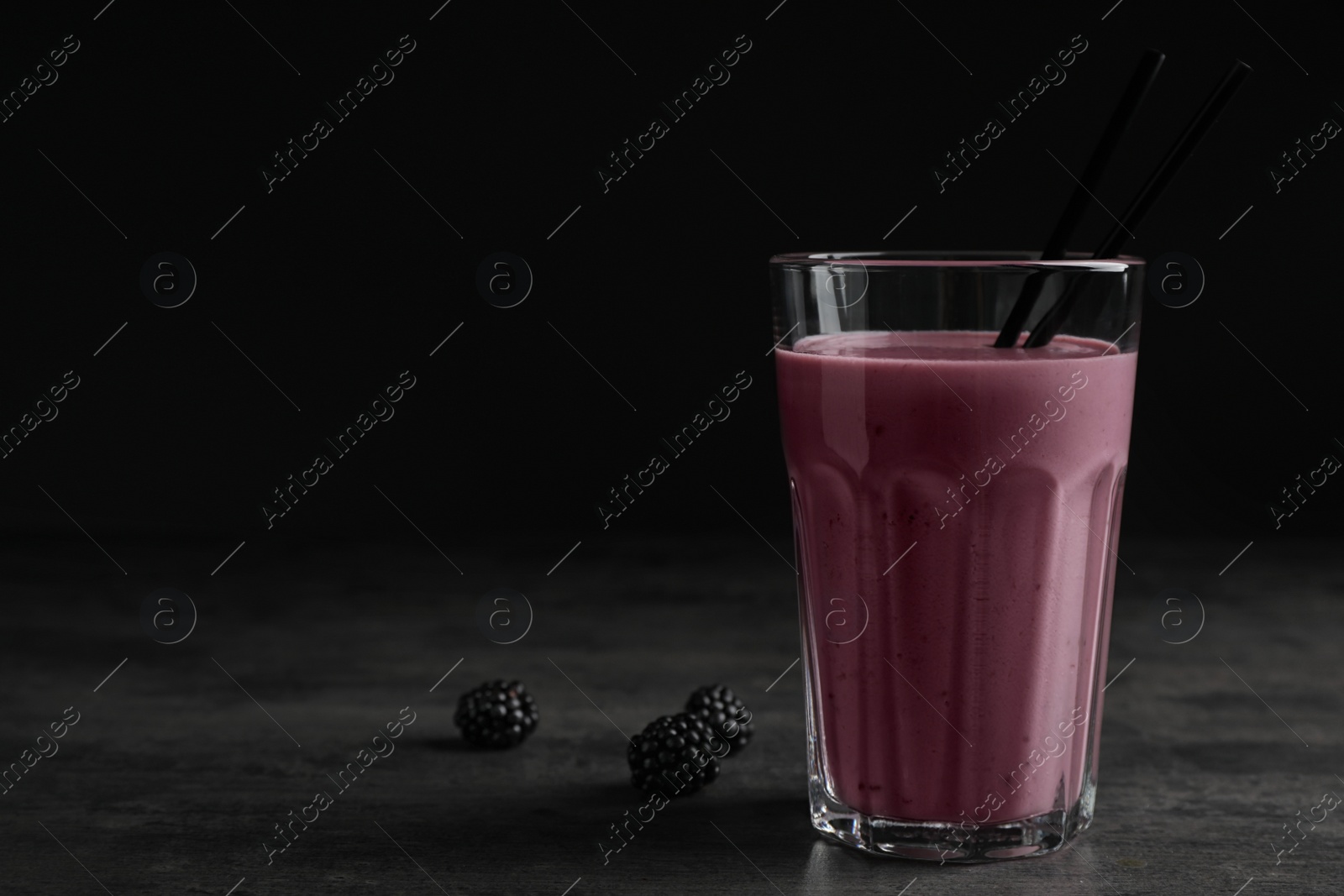 Photo of Glass with blackberry yogurt smoothie on grey table against dark background