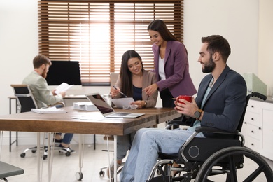 Young man in wheelchair with colleagues at workplace