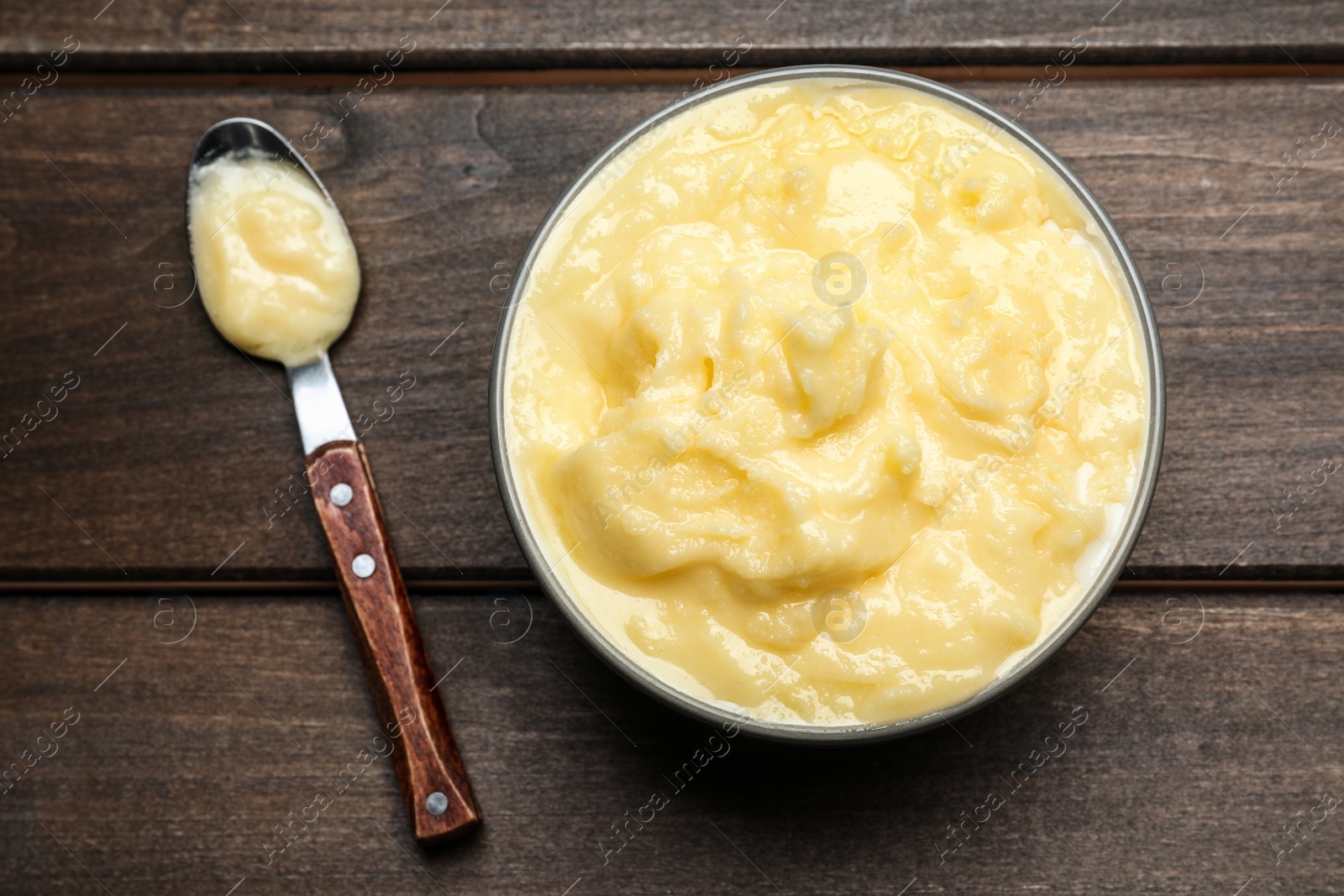 Photo of Bowl and spoon of Ghee butter on wooden table, flat lay