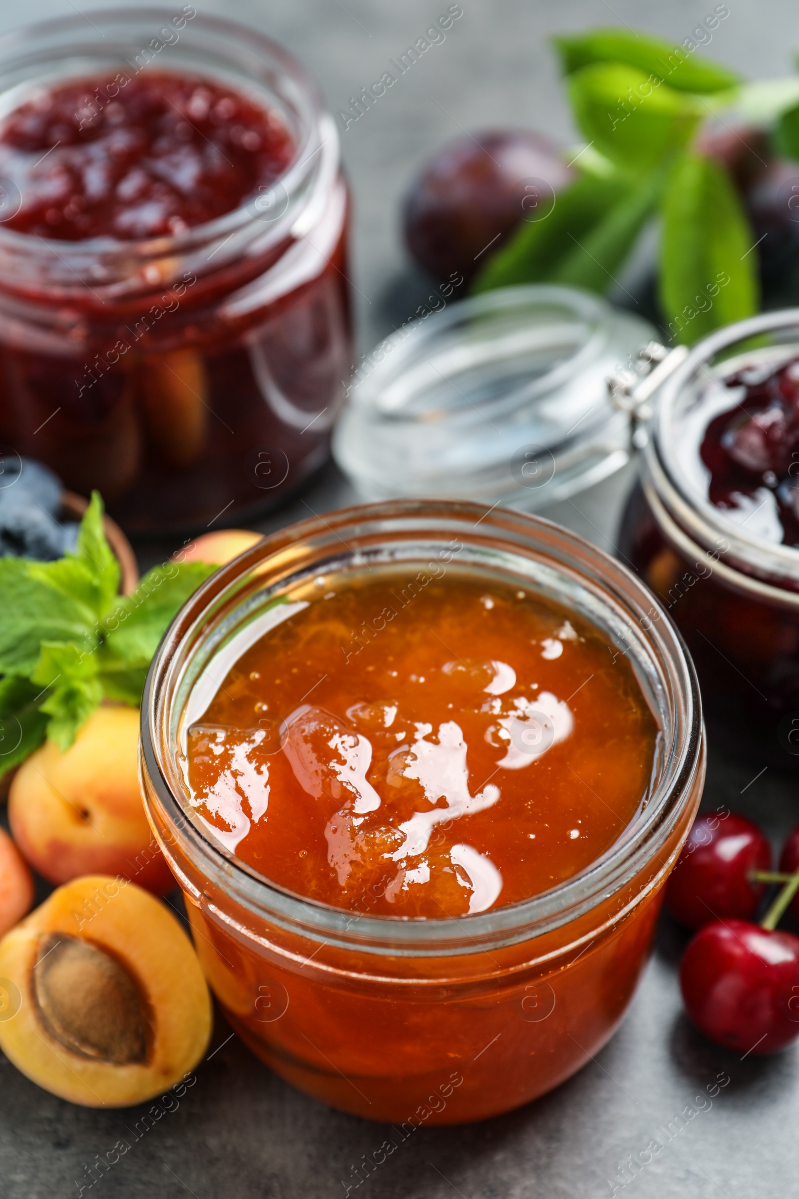Photo of Jars with different jams and fresh fruits on grey table, closeup