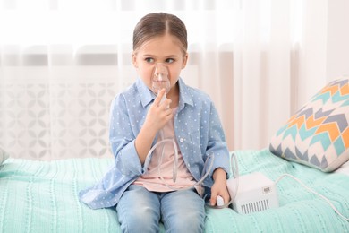 Photo of Sick little girl using nebulizer for inhalation on bed at home