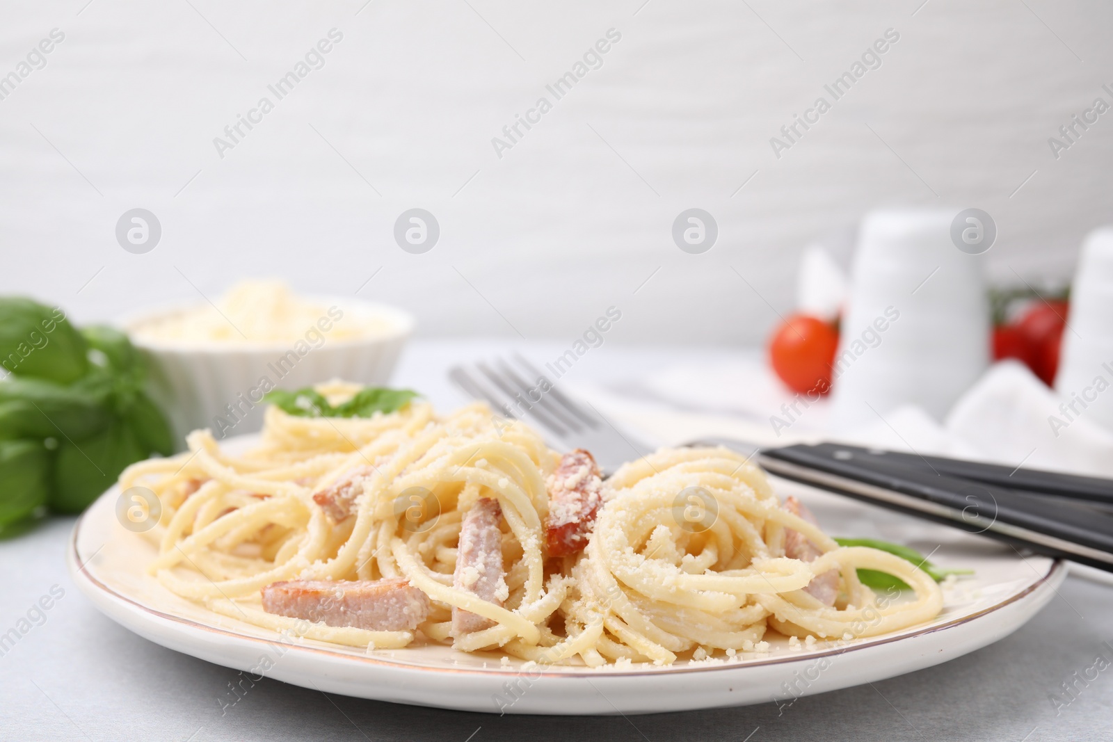 Photo of Plate of tasty pasta Carbonara with basil leaves on light grey table, closeup