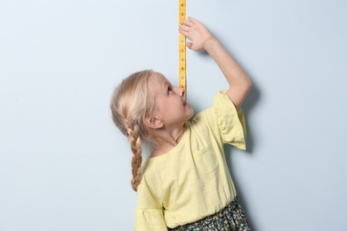 Photo of Little girl measuring her height on light background