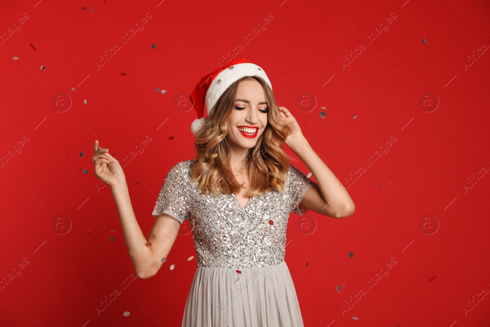 Photo of Happy young woman wearing Santa hat and confetti on red background. Christmas celebration