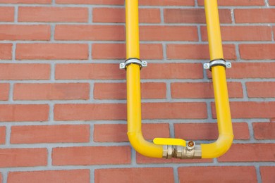 Yellow gas pipe on red brick wall outdoors, space for text