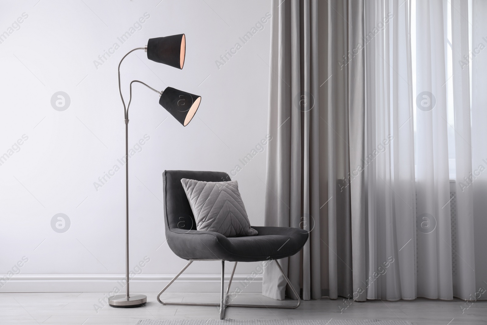 Photo of Comfortable armchair with cushion and floor lamp near white wall indoors