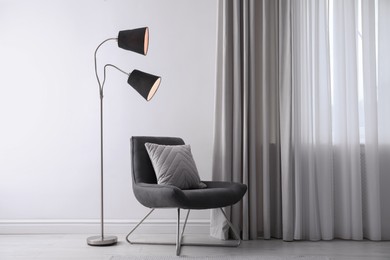 Photo of Comfortable armchair with cushion and floor lamp near white wall indoors