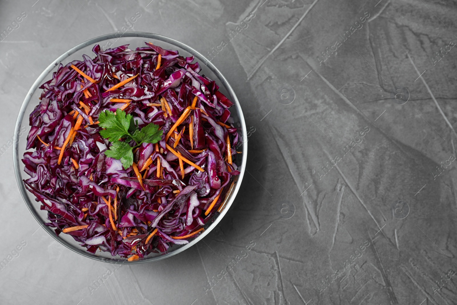 Photo of Bowl with fresh red cabbage salad on grey table, top view. Space for text