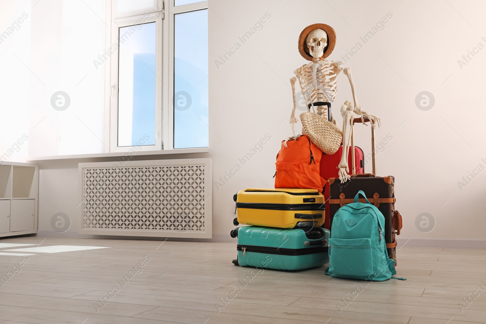 Photo of Waiting concept. Human skeleton in hat with suitcases indoors