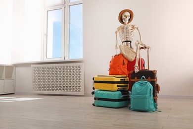 Photo of Waiting concept. Human skeleton in hat with suitcases indoors