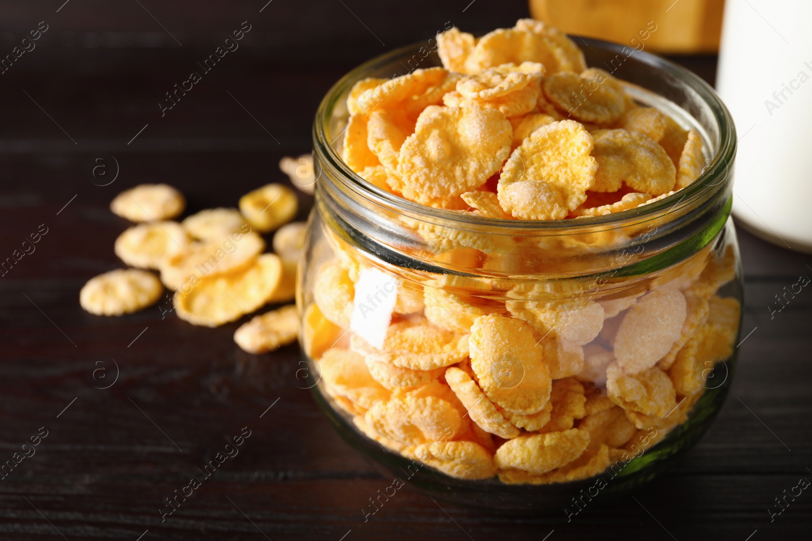 Photo of Jar of tasty crispy corn flakes on wooden table, closeup