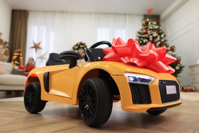 Photo of Children's electric toy car with red bow in room decorated for Christmas, low angle view