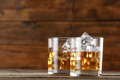 Photo of Whiskey with ice cubes in glasses on wooden table, closeup. Space for text