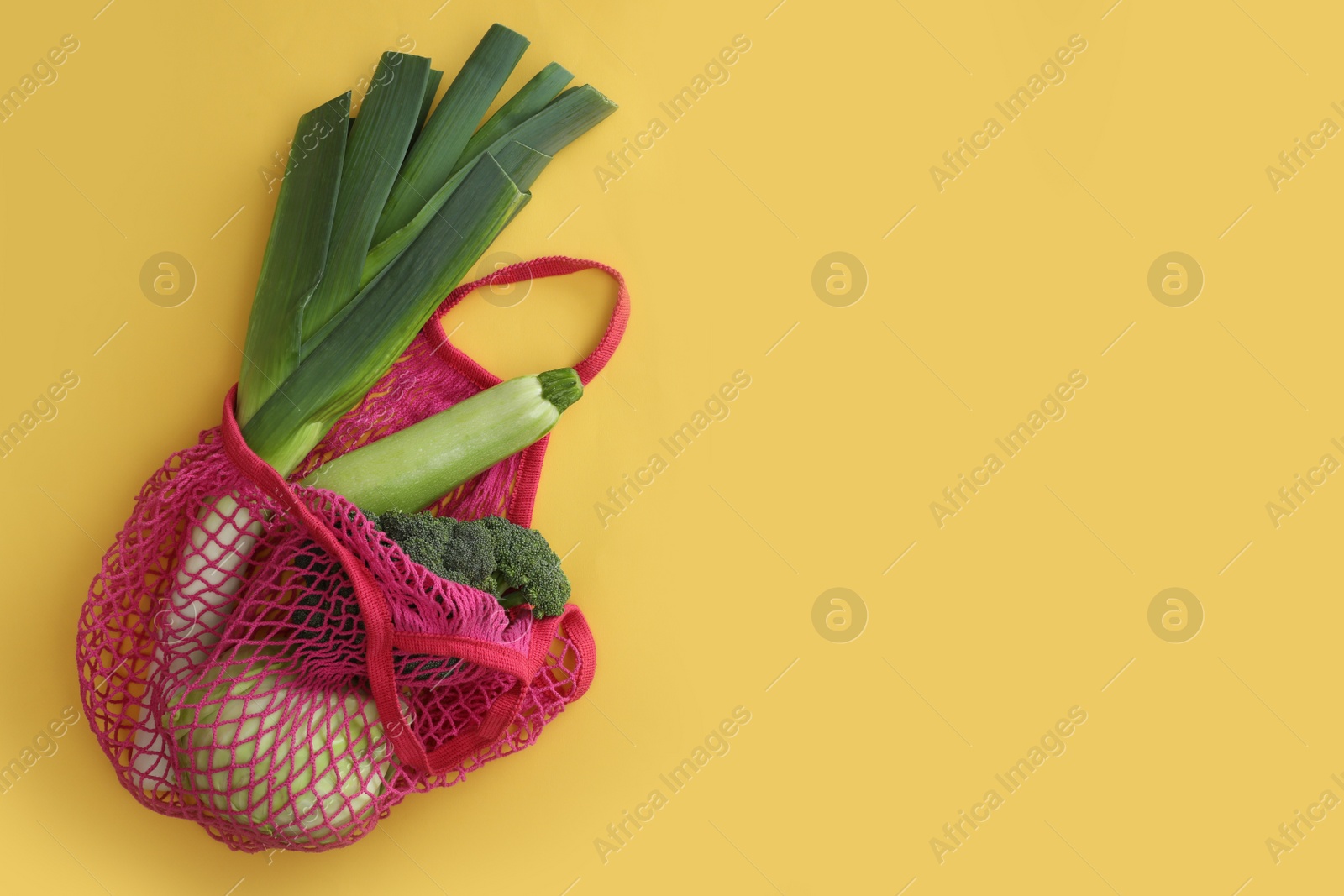 Photo of Net bag with vegetables on yellow background, top view. Space for text