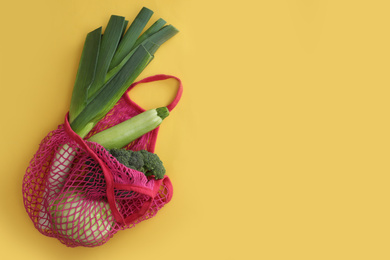 Photo of Net bag with vegetables on yellow background, top view. Space for text
