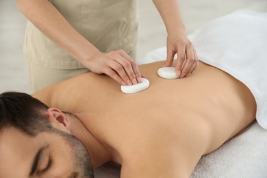 Man receiving hot stone massage in spa salon, closeup