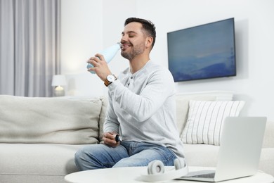 Man drinking from light blue thermo bottle indoors
