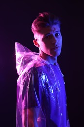 Photo of Young man wearing clear coat on dark background in neon lights