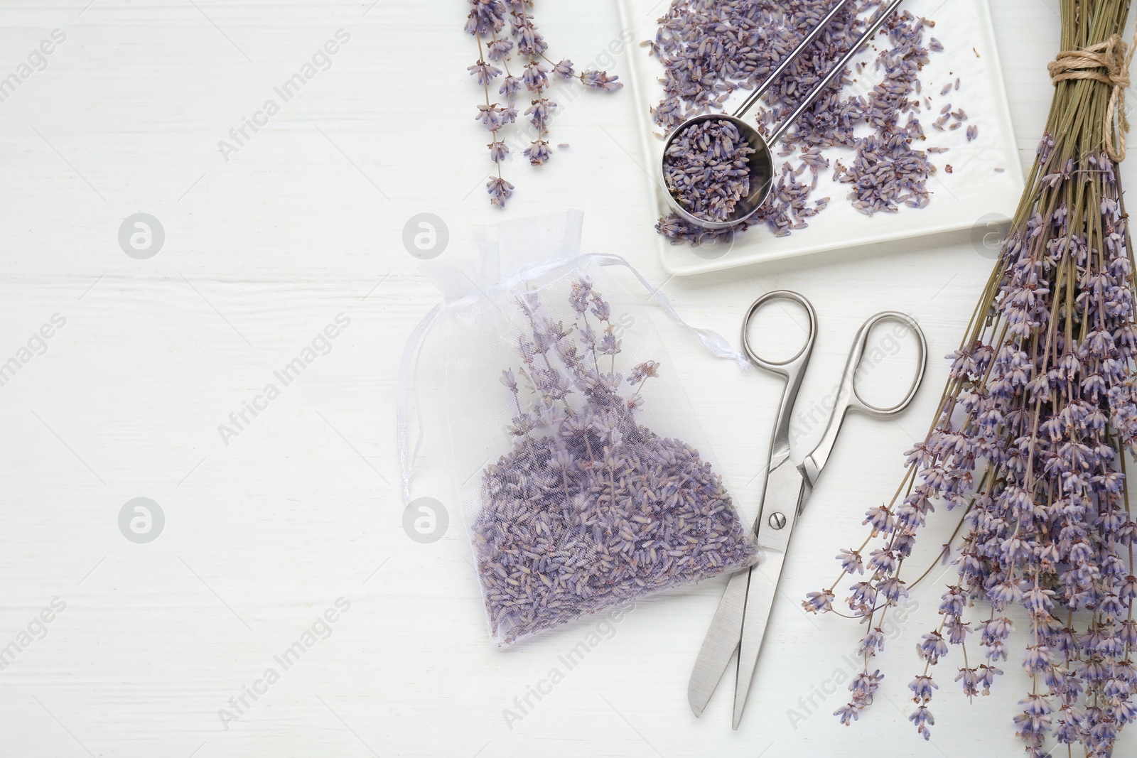 Photo of Scented sachet with dried lavender flowers and scissors on white wooden table, flat lay. Space for text