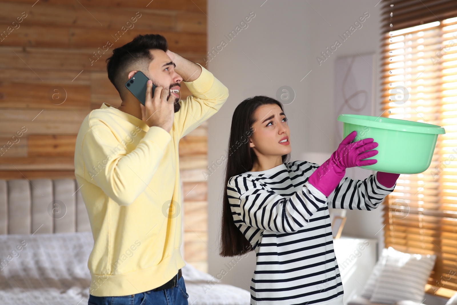 Photo of Young woman collecting leaking water from ceiling while her boyfriend calling roof repair service at home