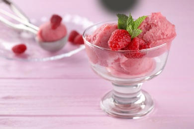 Photo of Delicious raspberry ice cream in dessert bowl on pink wooden table, closeup. Space for text