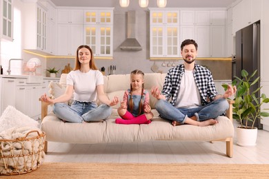 Photo of Family meditating together on sofa at home. Harmony and zen