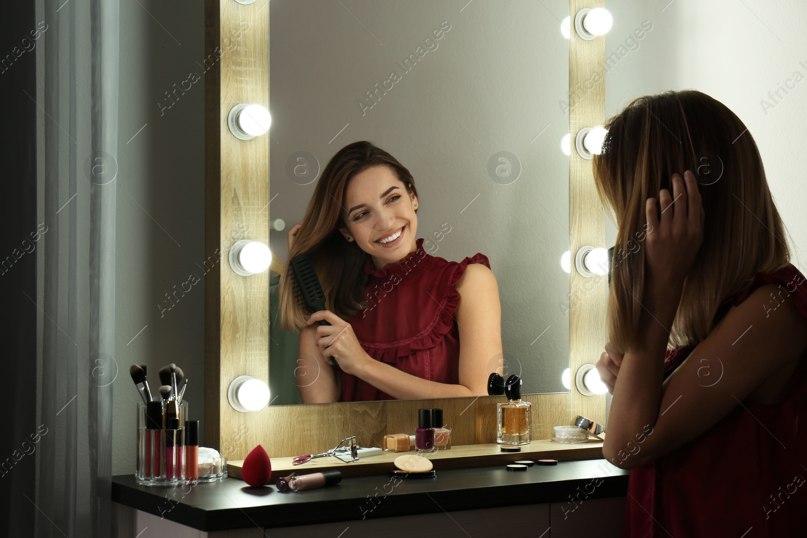 Photo of Woman brushing hair near mirror with light bulbs in dressing room