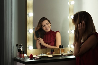 Woman brushing hair near mirror with light bulbs in dressing room