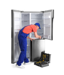 Male technician repairing refrigerator on white background