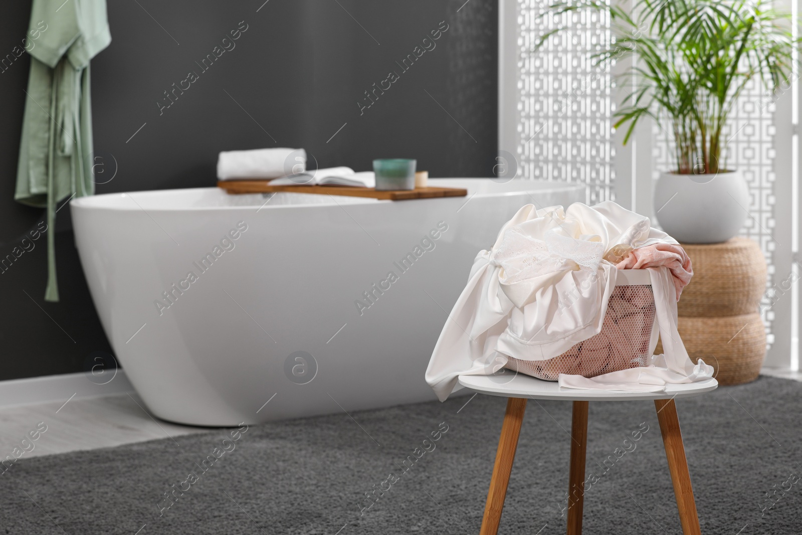 Photo of Laundry basket filled with clothes on table in bathroom. Space for text