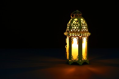 Photo of Decorative Arabic lantern on table against dark background. Space for text