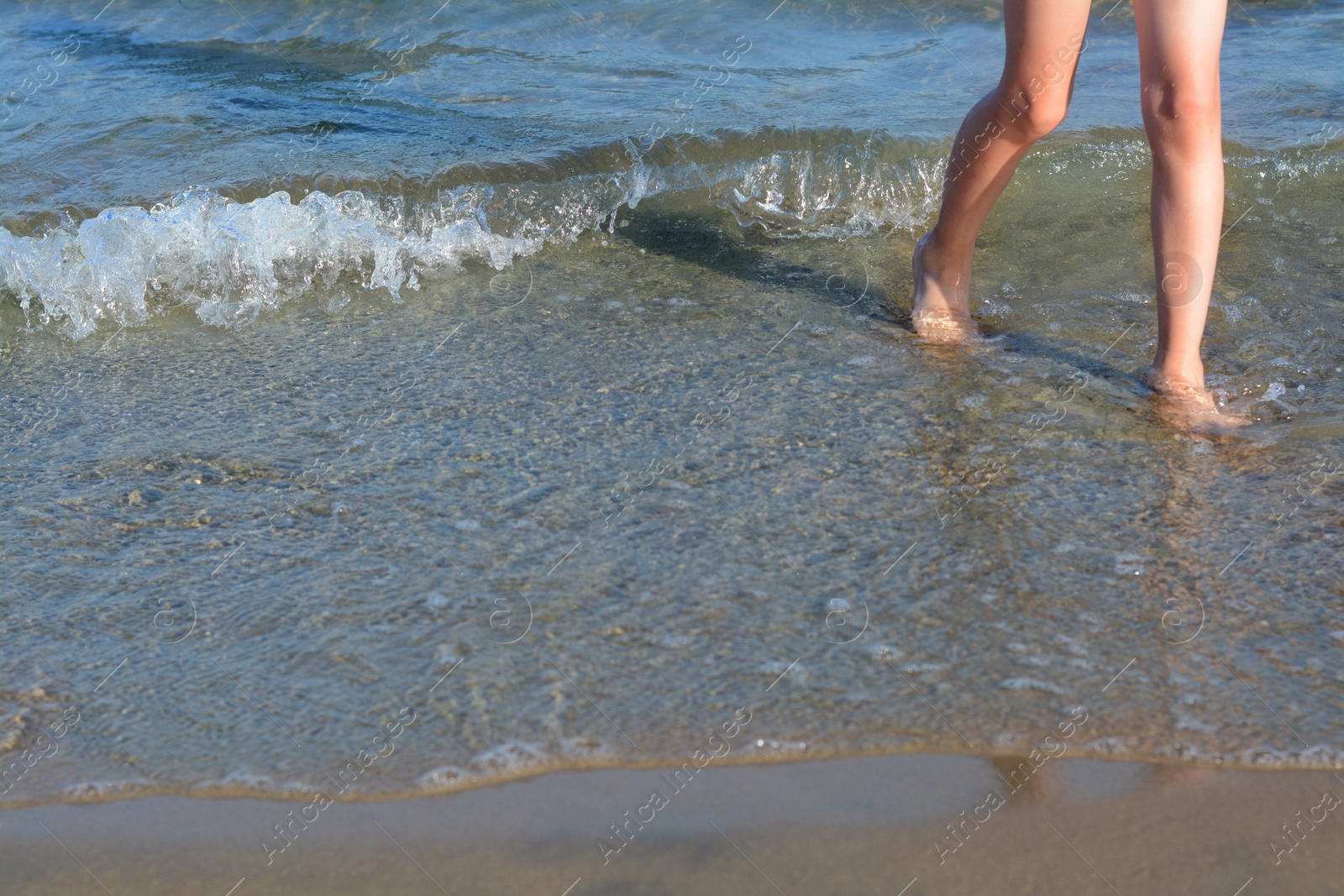 Photo of Child walking through water on seashore, closeup of legs