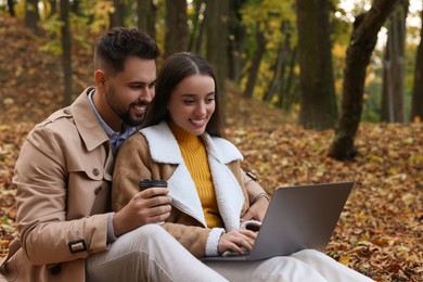 Happy young couple with laptop spending time together in autumn park