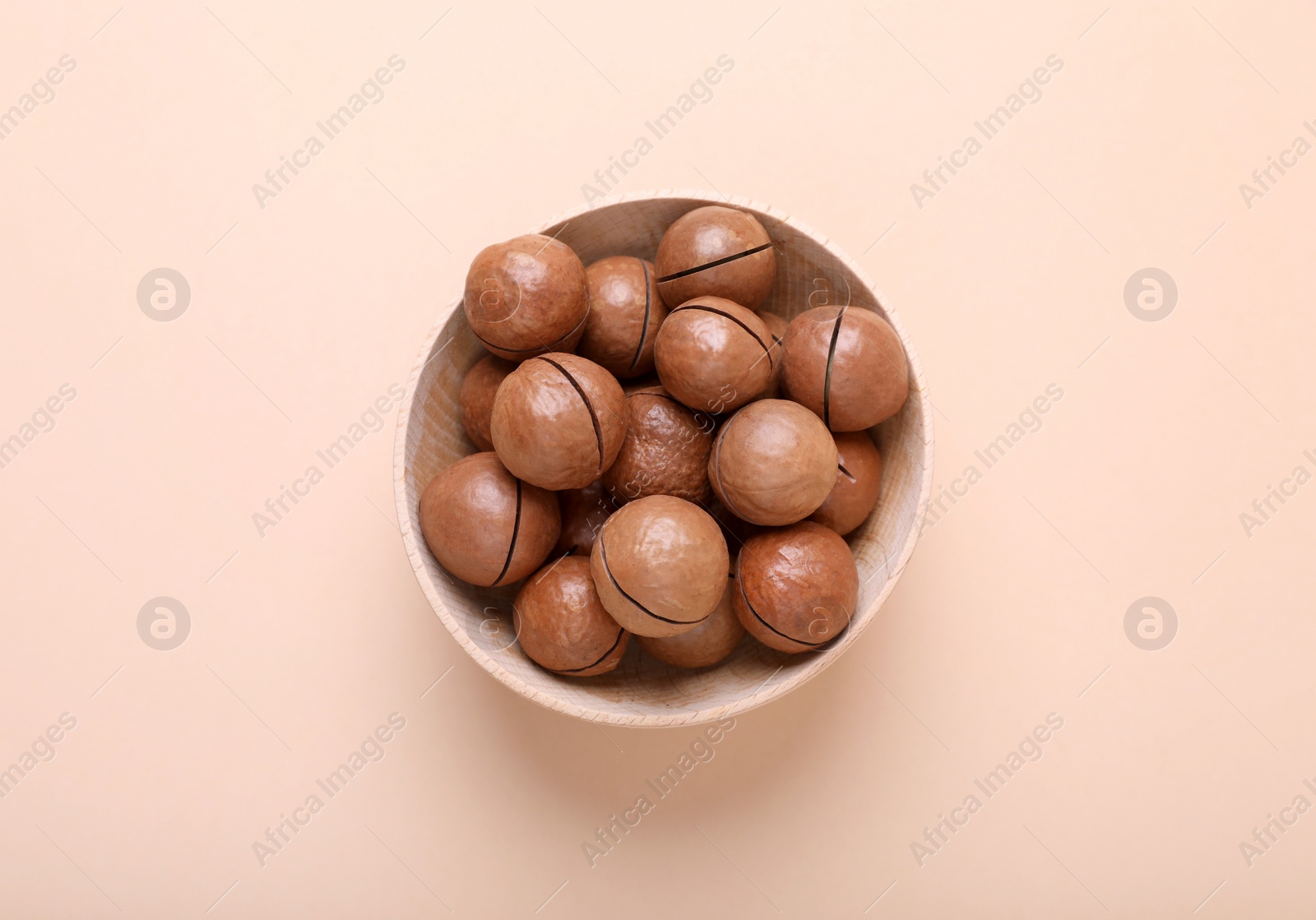 Photo of Delicious organic Macadamia nuts in wooden bowl on beige background, top view