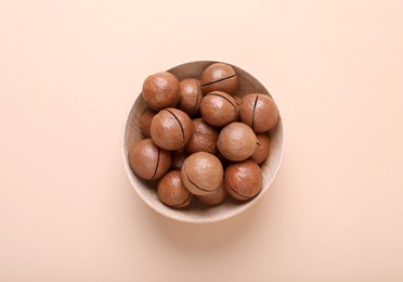 Photo of Delicious organic Macadamia nuts in wooden bowl on beige background, top view