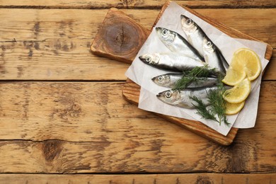 Photo of Fresh raw sprats, lemon and dill on wooden table, top view. Space for text