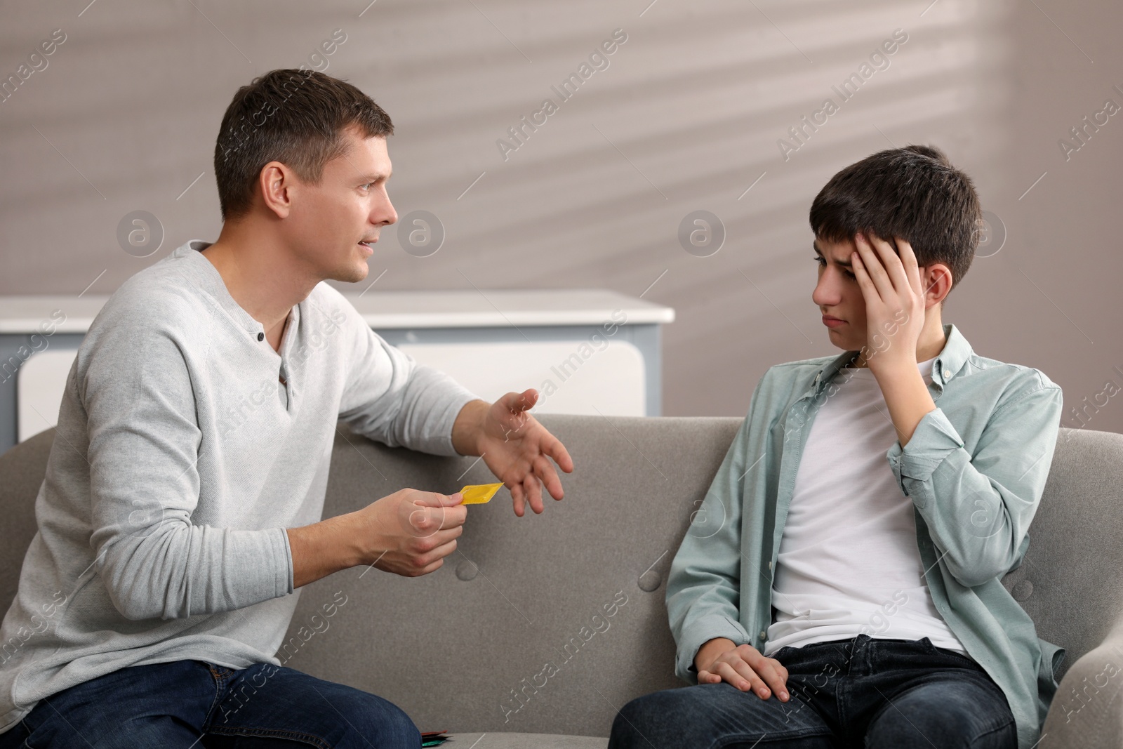 Photo of Father talking with his teenage son about contraception at home. Sex education concept