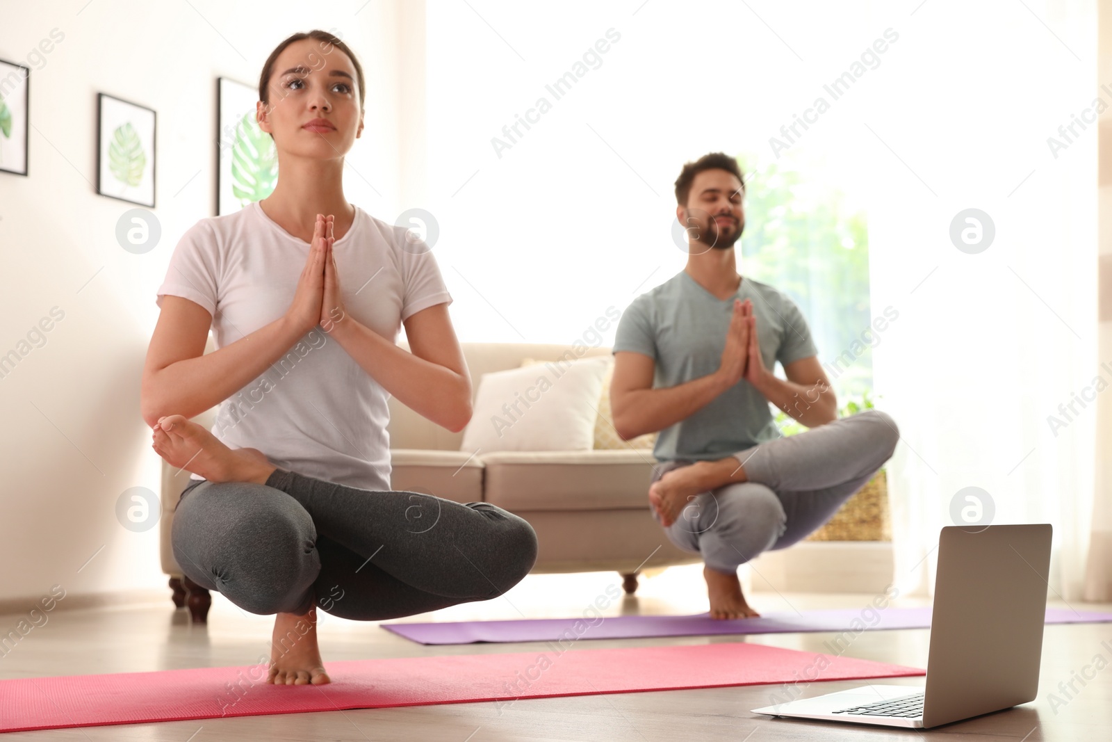 Photo of Couple practicing yoga while watching online class at home during coronavirus pandemic. Social distancing