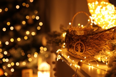 Photo of Fireplace mantel with wicker basket, festive lights and blurred Christmas tree on background
