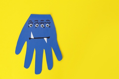 Photo of Funny blue hand shaped monster on yellow background, top view with space for text. Halloween decoration