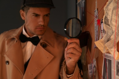 Photo of Old fashioned detective with magnifying glass near investigation board in office