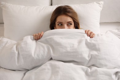Photo of Woman hiding under warm white blanket in bed, above view
