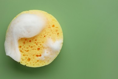 Yellow sponge with foam on green background, top view. Space for text