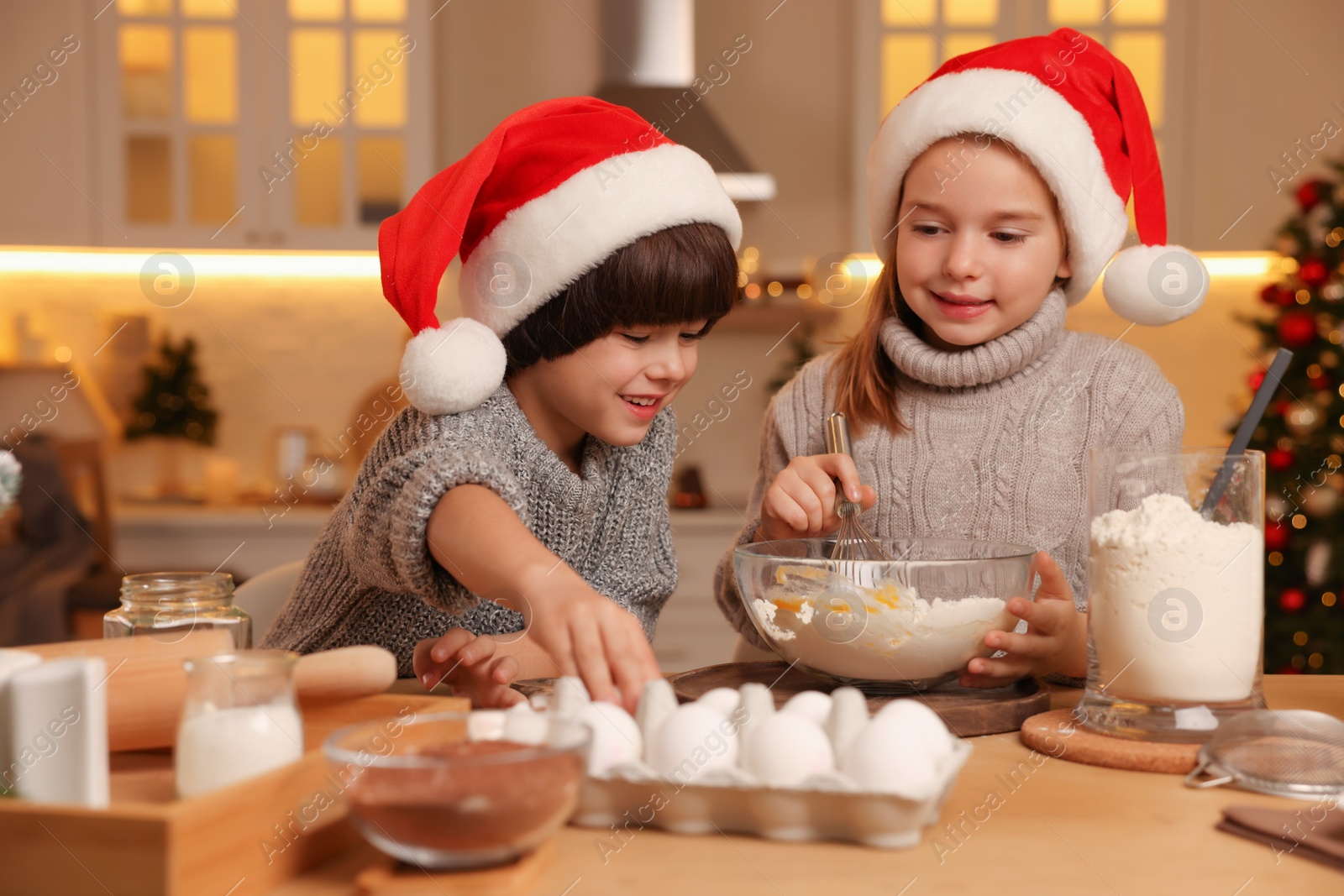 Photo of Cute little children making dough for Christmas cookies in kitchen