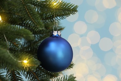 Photo of Beautiful blue bauble hanging on Christmas tree against blurred festive lights, closeup