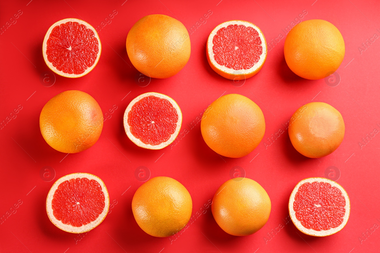 Photo of Cut and whole ripe grapefruits on red background, flat lay