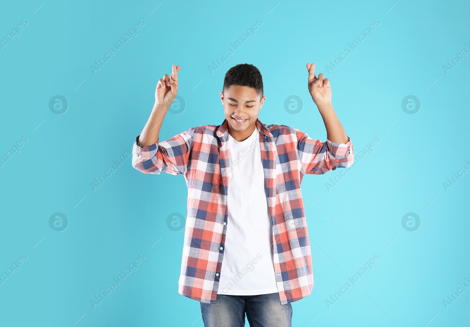 Photo of African-American teenage boy crossing his fingers on color background